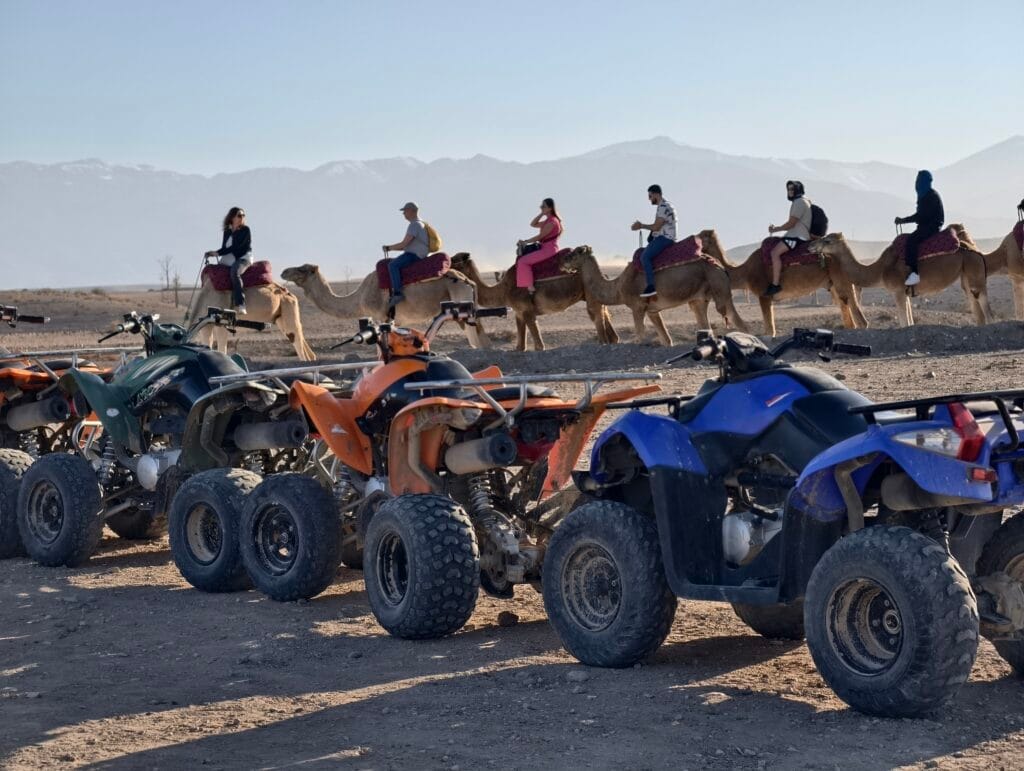Quad bikes and a camel caravan in the Agafay desert with the Atlas Mountains behind