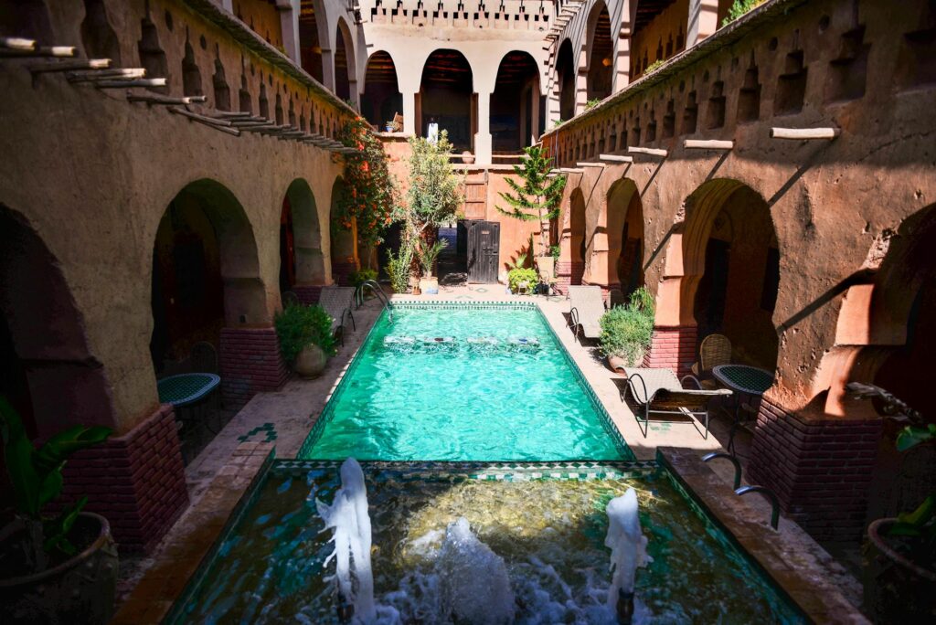 A luxury courtyard featuring a gorgeous premium riad marrakech private pool surrounded by green plants and traditional Moroccan zellige tiles